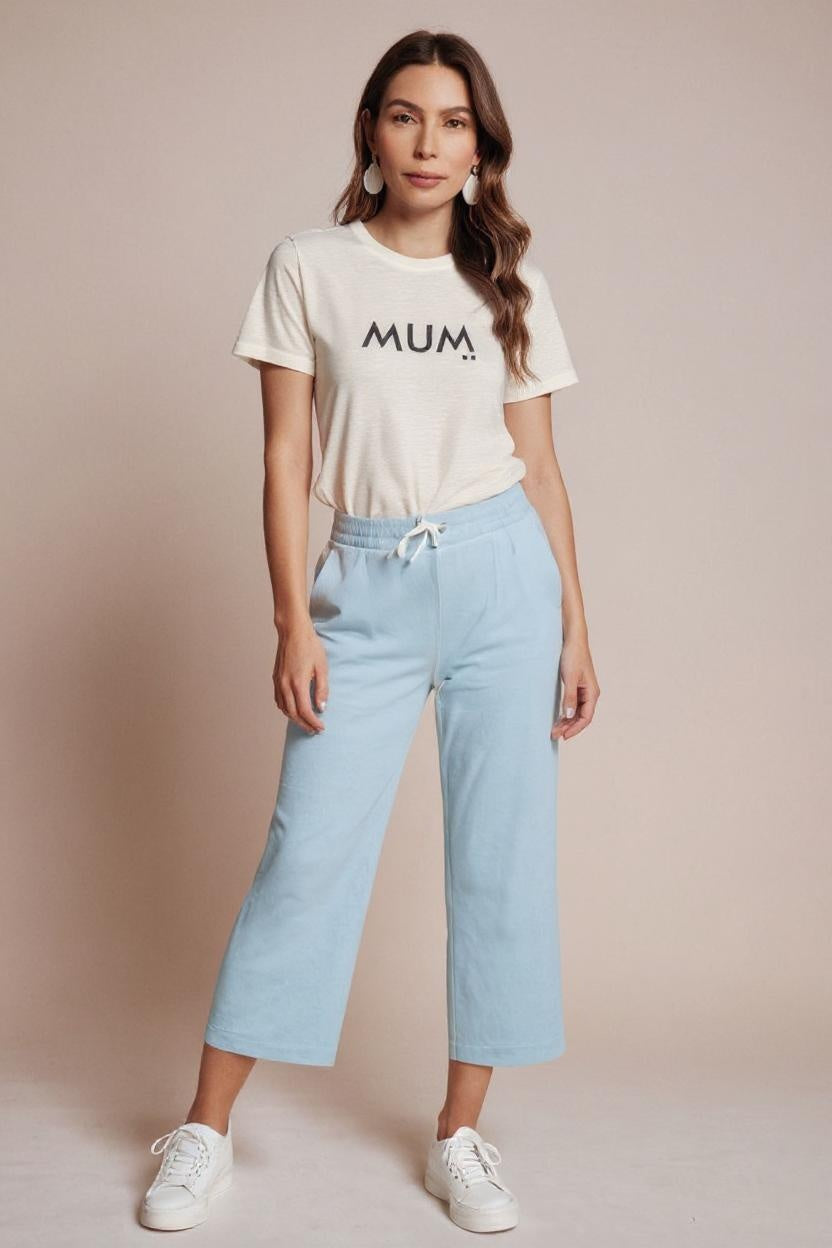 Woman wearing a white t-shirt with 'MUM' text and light blue jeans on a beige background