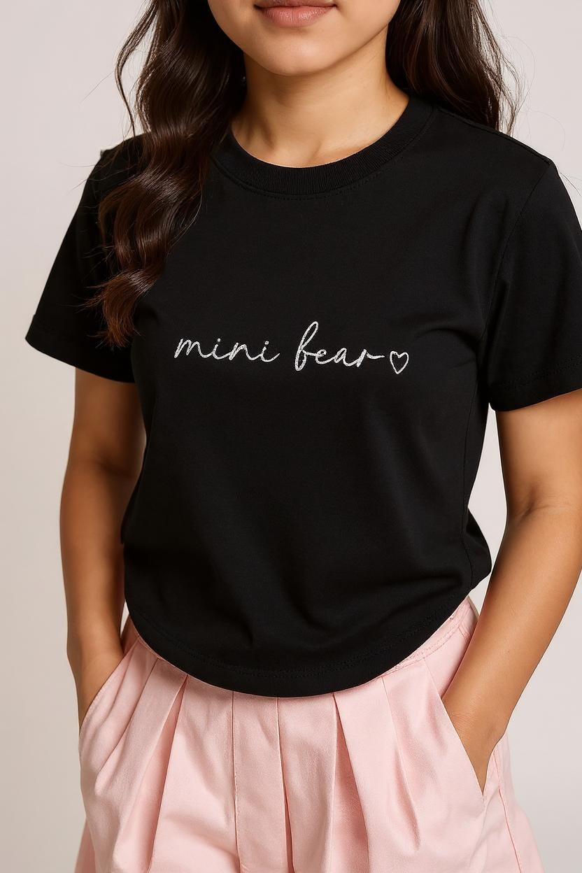 Person wearing a black t-shirt with 'mini bear' text and a heart on a plain background