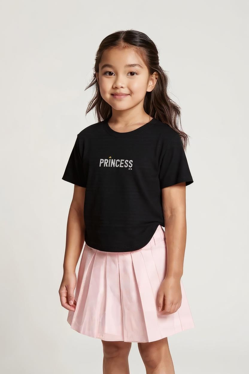 Young girl wearing a black 'PRINCESS' t-shirt and pink skirt on a light gray background