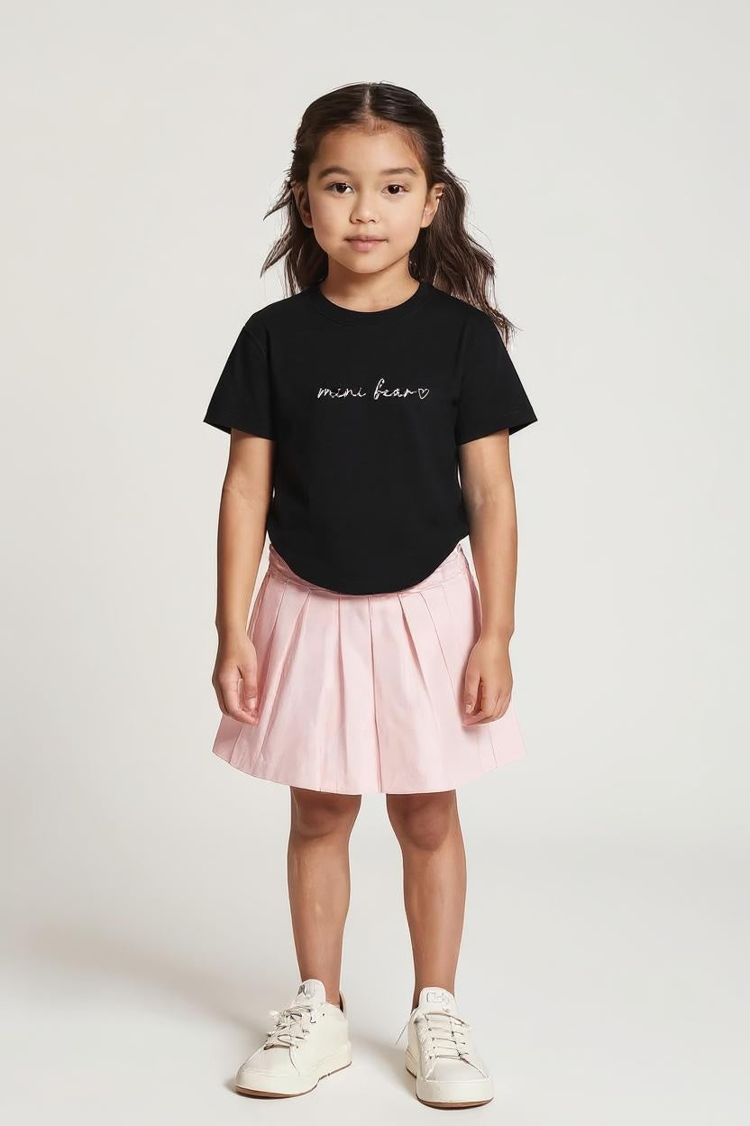 Young girl wearing a black t-shirt with text and a pink skirt on a white background