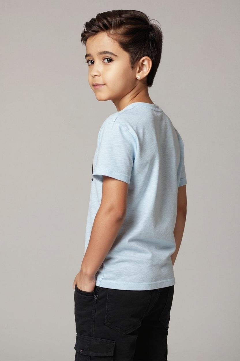Young boy wearing a light blue t-shirt and dark pants against a plain background