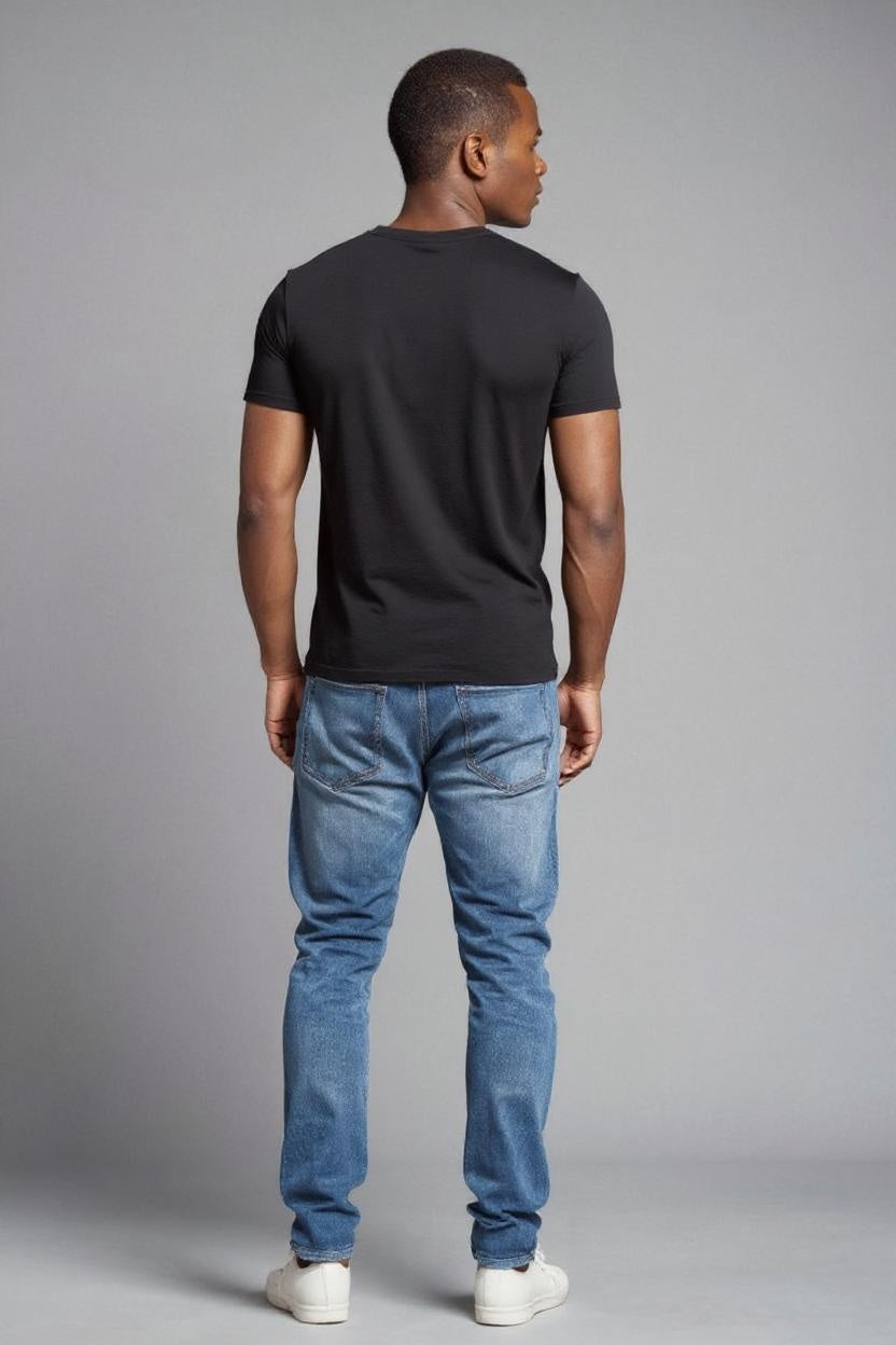 Man wearing a black t-shirt and blue jeans against a gray background
