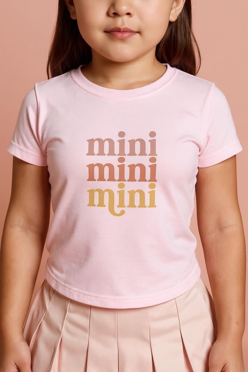 Child wearing a pink t-shirt with 'mini mini mini' text on a peach background
