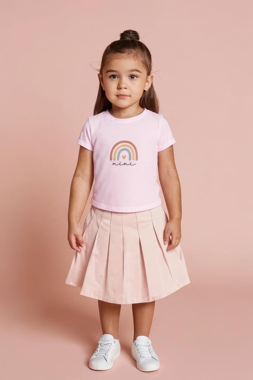 Young girl wearing a pink t-shirt with a rainbow design and pleated skirt on a pink background