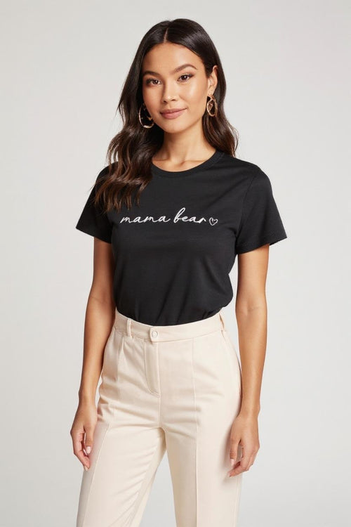 Woman wearing a black 'mama bear' t-shirt and beige pants on a white background