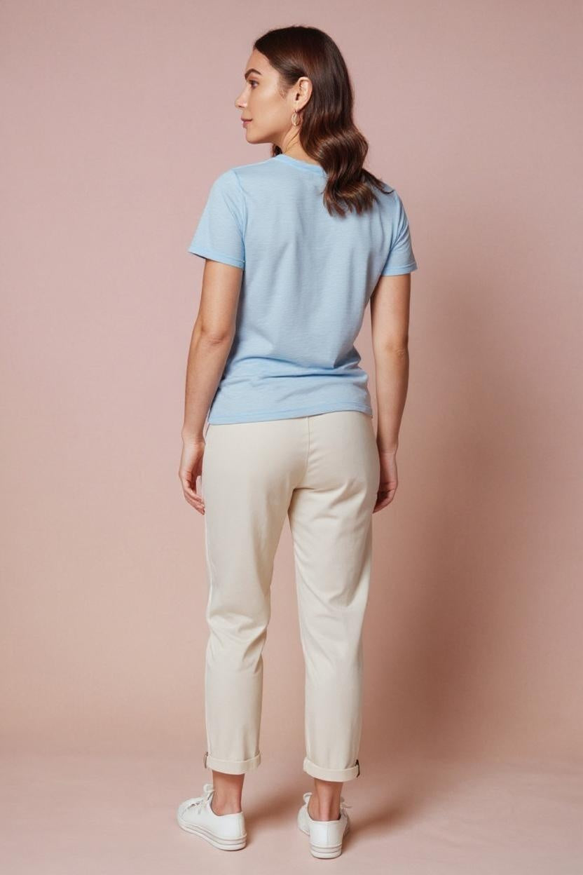 Woman wearing a light blue t-shirt and beige pants against a pink background