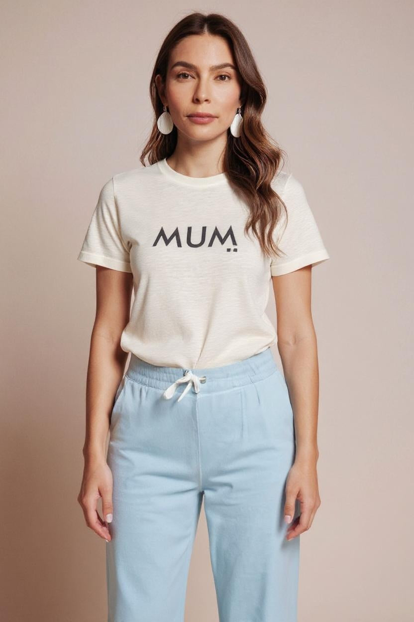 Woman wearing a white t-shirt with 'MUM' text and light blue pants on a beige background