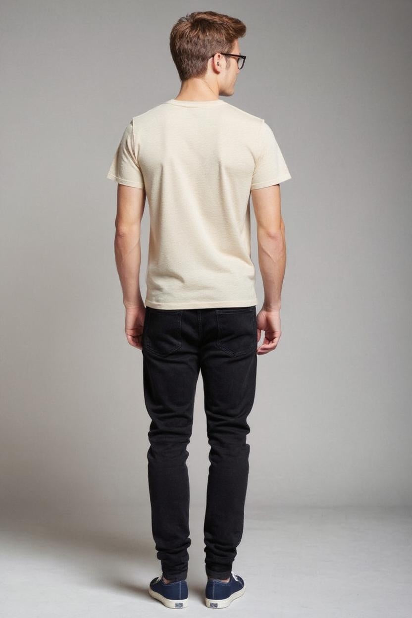 Man wearing a beige t-shirt and black jeans against a gray background