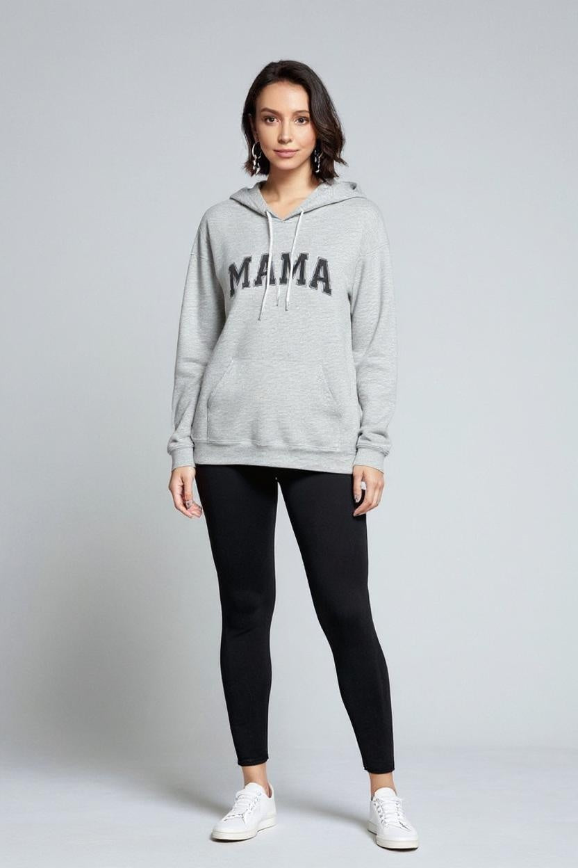 Woman wearing a gray hoodie with 'MAMA' text and black leggings on a light gray background