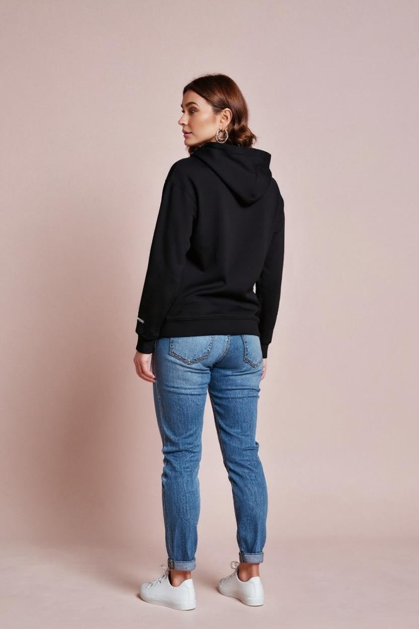 Person wearing a black hoodie and blue jeans on a beige background