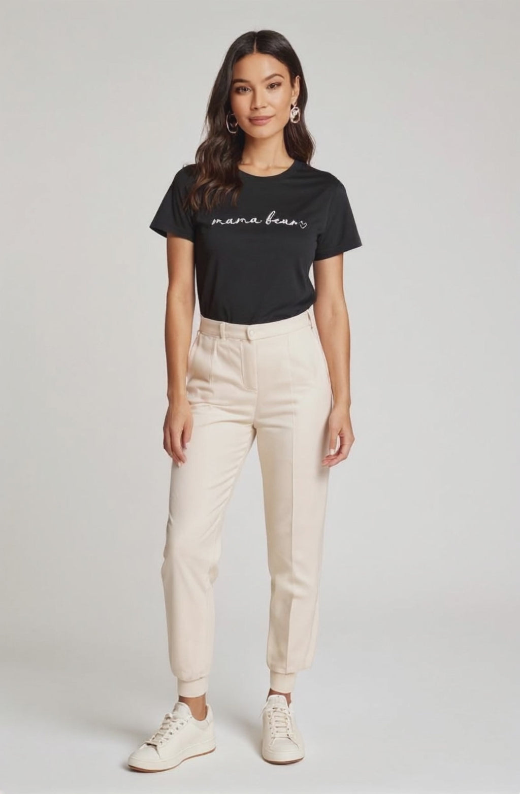 Woman wearing a black 'mama bear' t-shirt and beige pants on a white background